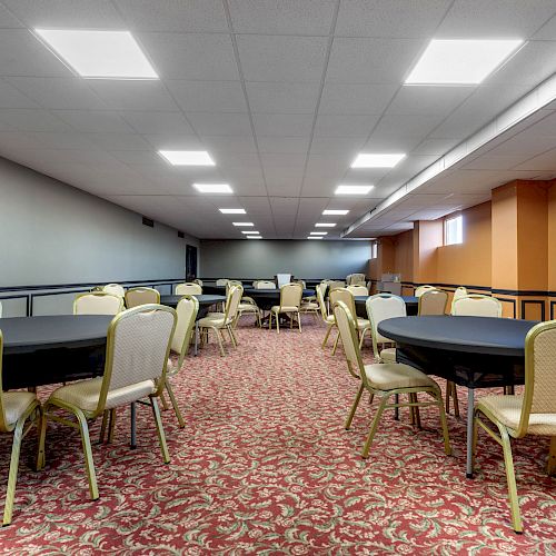 The image shows a room with round tables and chairs on a patterned carpet, likely set up for a meeting, banquet, or conference event.