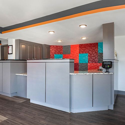 The image shows a modern reception desk area with a colorful back wall, gray counters, bright lighting, and a signboard on the right wall.