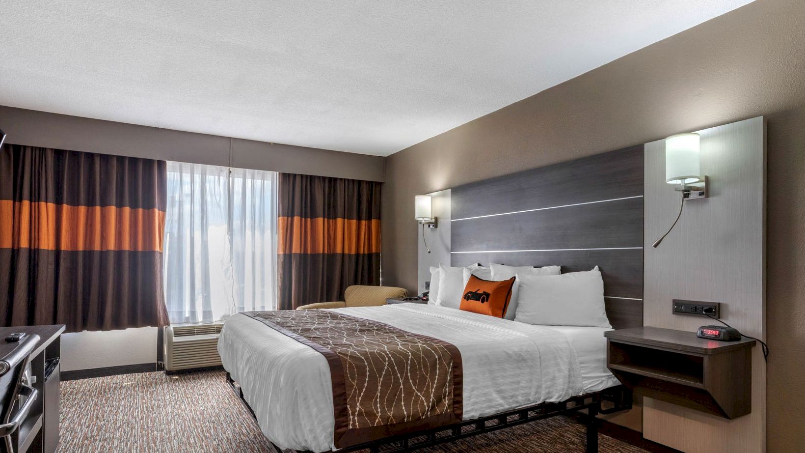 A modern hotel room with a king-sized bed, wall-mounted TV, desk, and two nightstands. The window has dark curtains with orange accents.