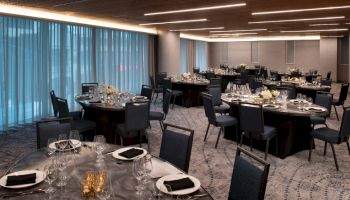 A modern, elegantly set banquet hall with round tables, dark chairs, and dim lighting, ready for an event or formal dinner.