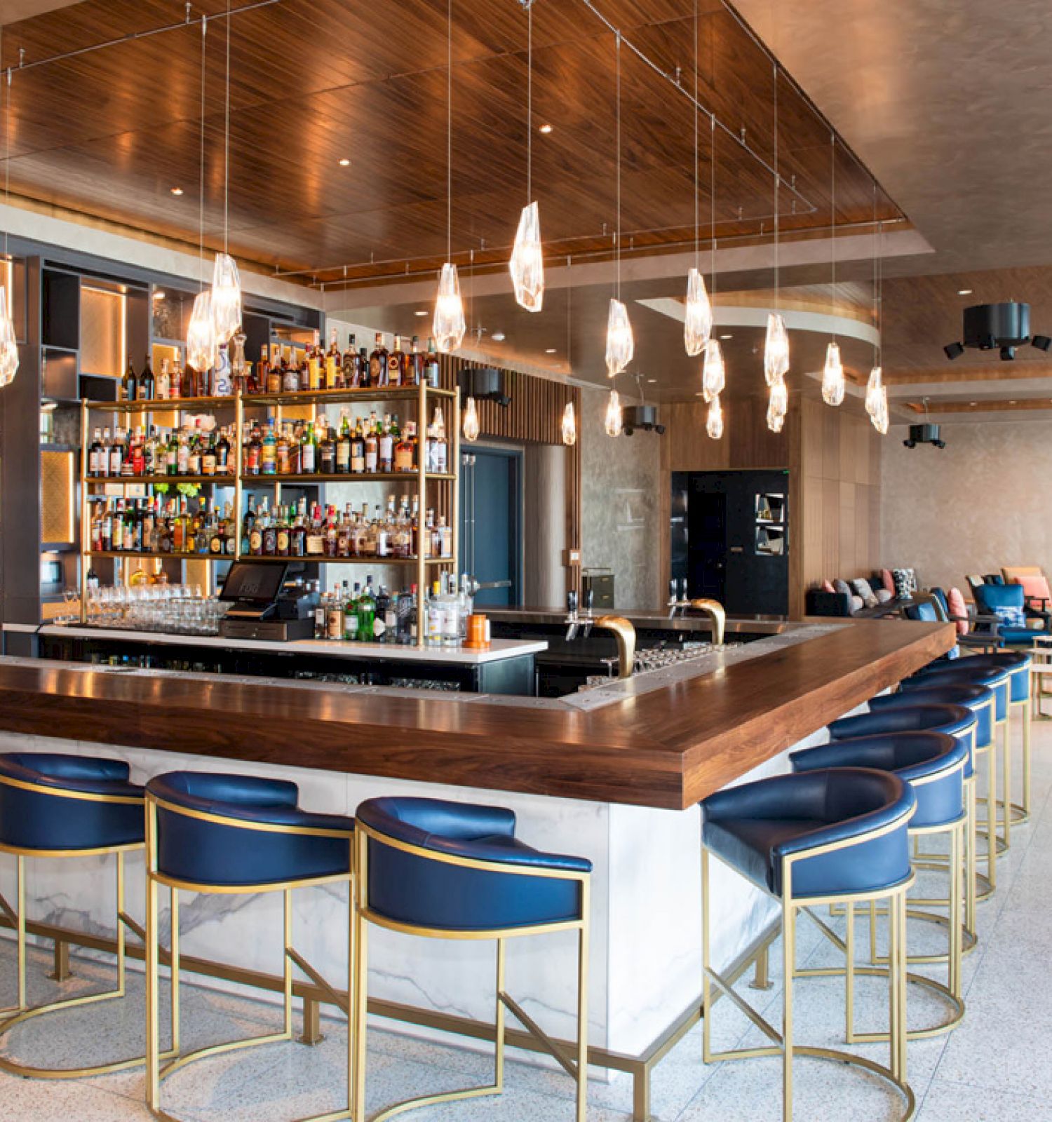 This image shows a modern bar with high chairs, a well-stocked liquor shelf, and stylish lighting decor, set within a spacious and stylish lounge.