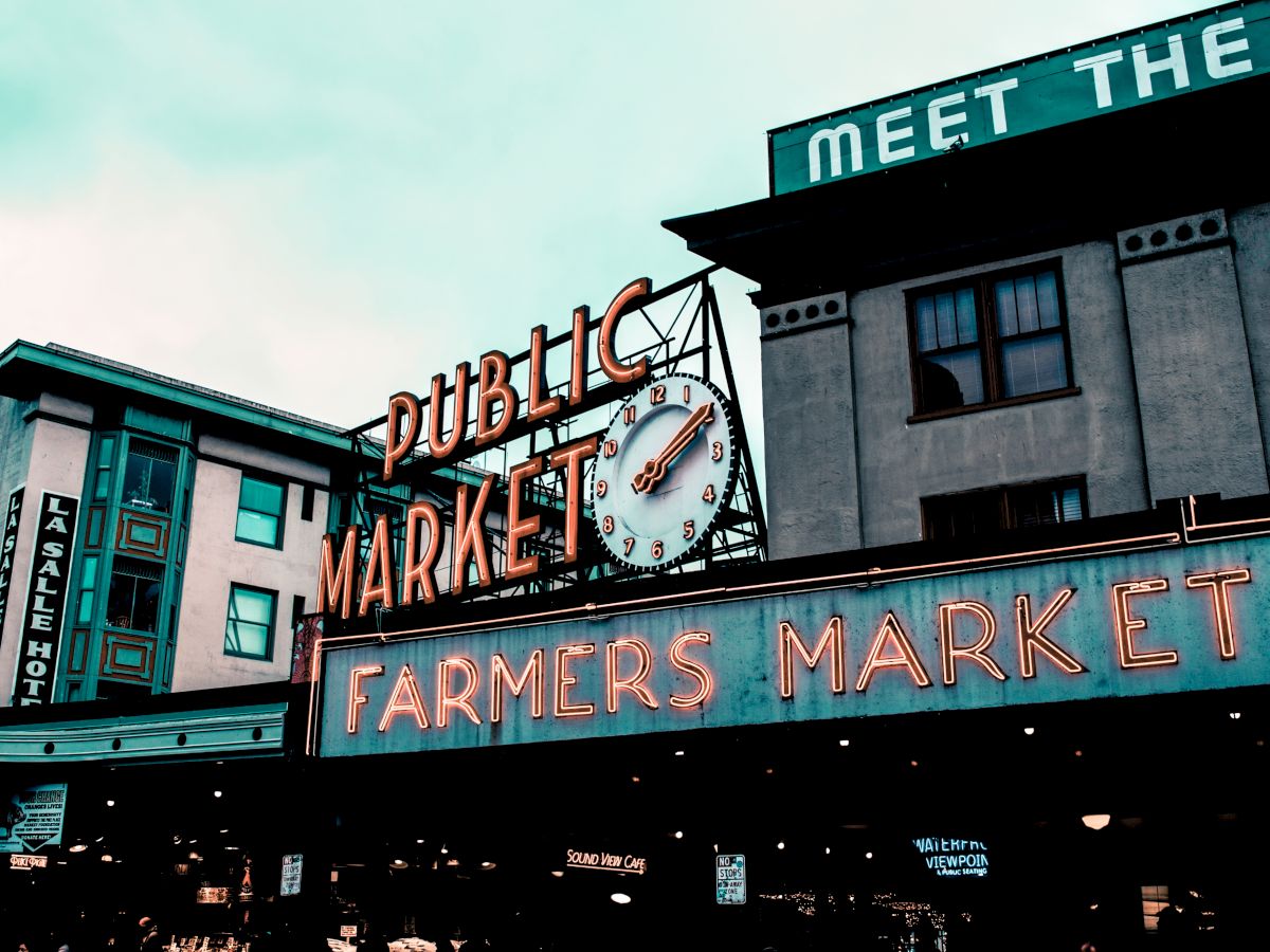 This image shows the signage for a "Public Market" and "Farmers Market" with a clock in the center, set on a rectangular building with a partly visible sign.