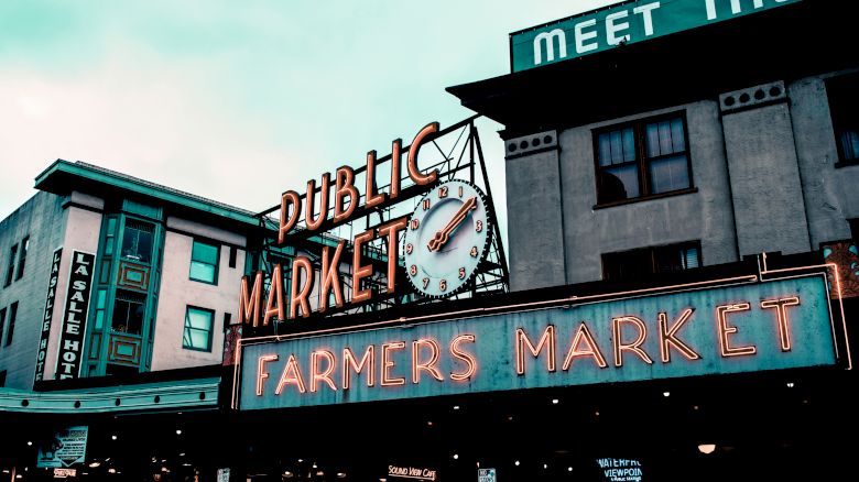 This image shows the signage for a "Public Market" and "Farmers Market" with a clock in the center, set on a rectangular building with a partly visible sign.