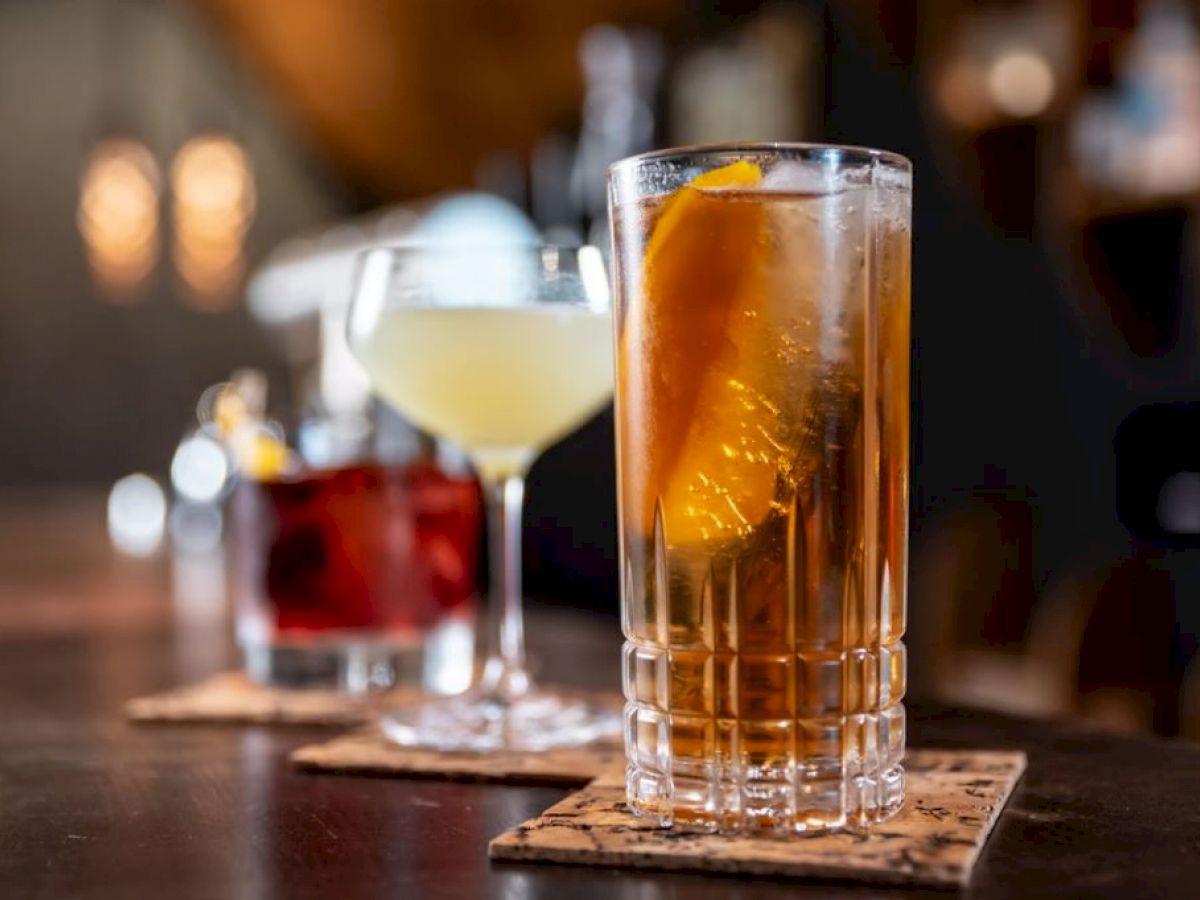 Three cocktails on a bar counter, each on a coaster; one with an orange slice.