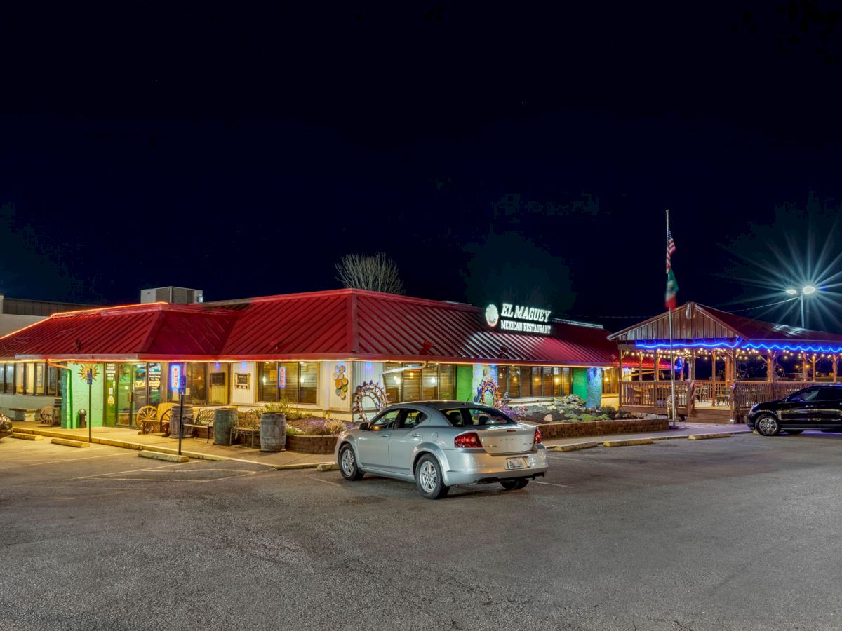 A brightly lit restaurant with a red roof and parking lot at night, featuring a few cars parked in front and illuminated outdoor seating.